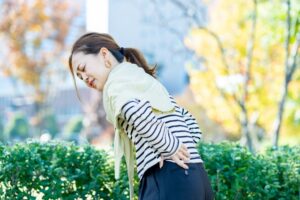 屋外で立ち止まり腰を押さえる女性